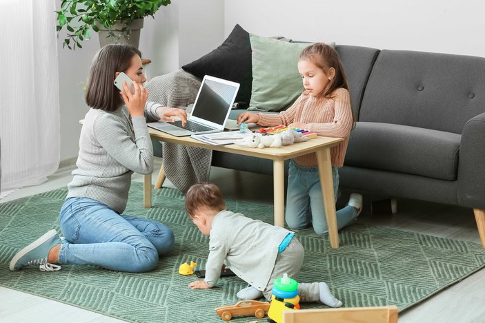 Mutter arbeite am Wohnzimmertisch am Notebook und Kinder spielen daneben