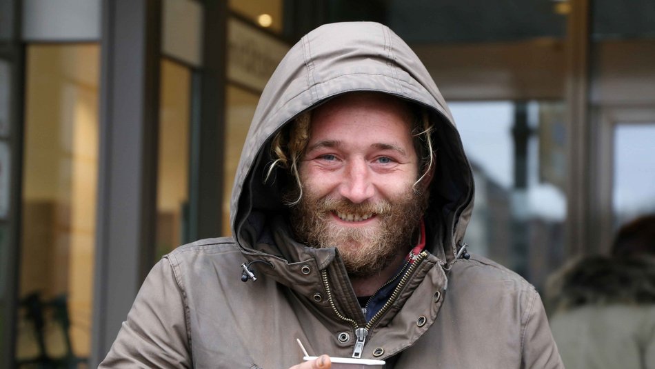 Mann mit Bart und Kapuze lacht und hält einen Pappbecher in der Hand