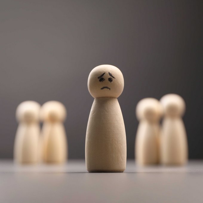 Eine Holsspielfigur mit traurigem Gesicht steht abseits anderer Holzspielfiguren