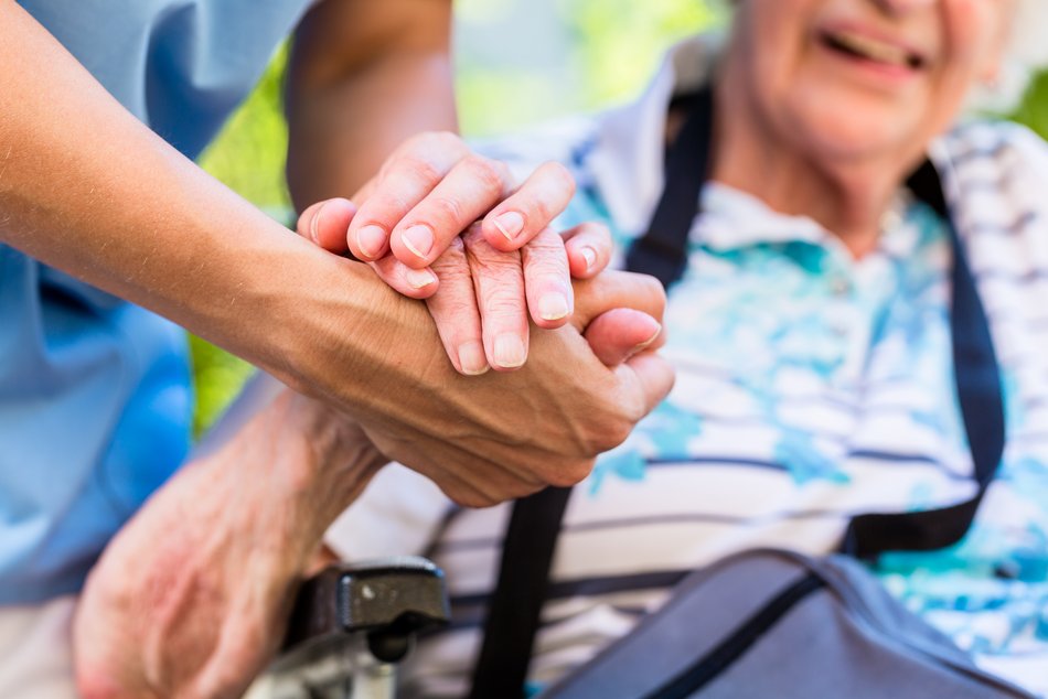 Pflegekraft hält Hände einer alten Person