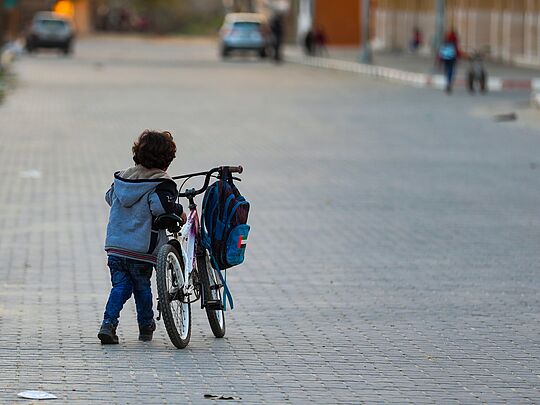 Ein kleines Kind schiebt ein Fahrad einsam über eine Straße.