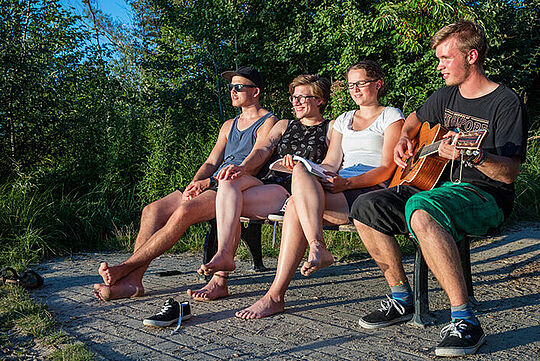 Freiwilliges soziales Jahr,  - vier junge Menschen sitzen auf einer Bank im Freien, einer spielt Gitarre.