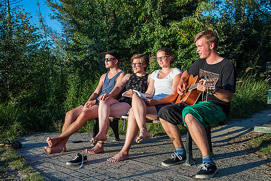 Freiwilliges soziales Jahr,  - vier junge Menschen sitzen auf einer Bank im Freien, einer spielt Gitarre.