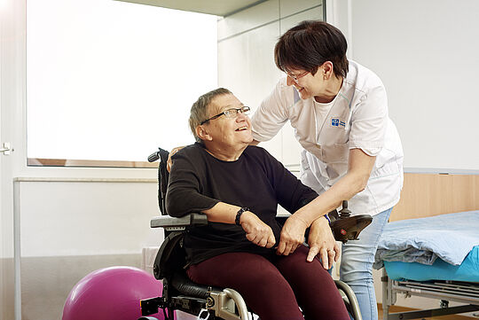 Pflegerin lächelt Frau in Rollstuhl an